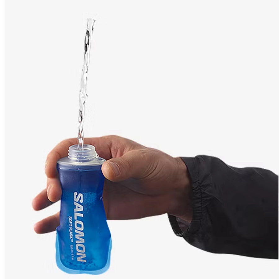 Hand holding a blue Salomon water bottle with water being poured from it on a white background